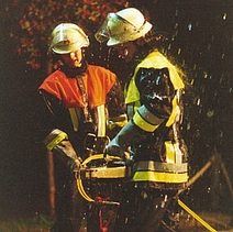 Zwei Feuerwehrmänner mit Schlauch bei Nässe.