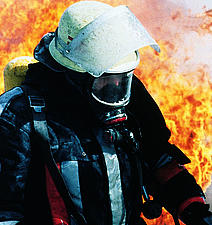 Ein Feuerwehrmann mit Atemmaske bewegt sich vor einem großen Feuer.